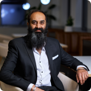 Kalwant, our Independent Audit Committee member, wearing a professional suit sat on a chair facing forward, smiling.