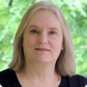 Julie has shoulder length, light coloured hair and wears a navy top and is smiling towards the camera outside MHA office.